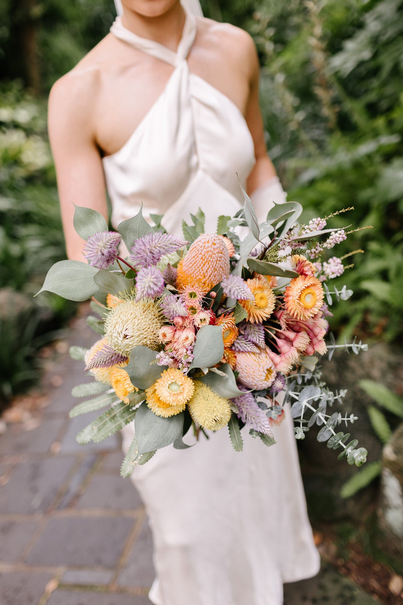 Bride holding a colorful native bouquet with greenery in a natural setting
