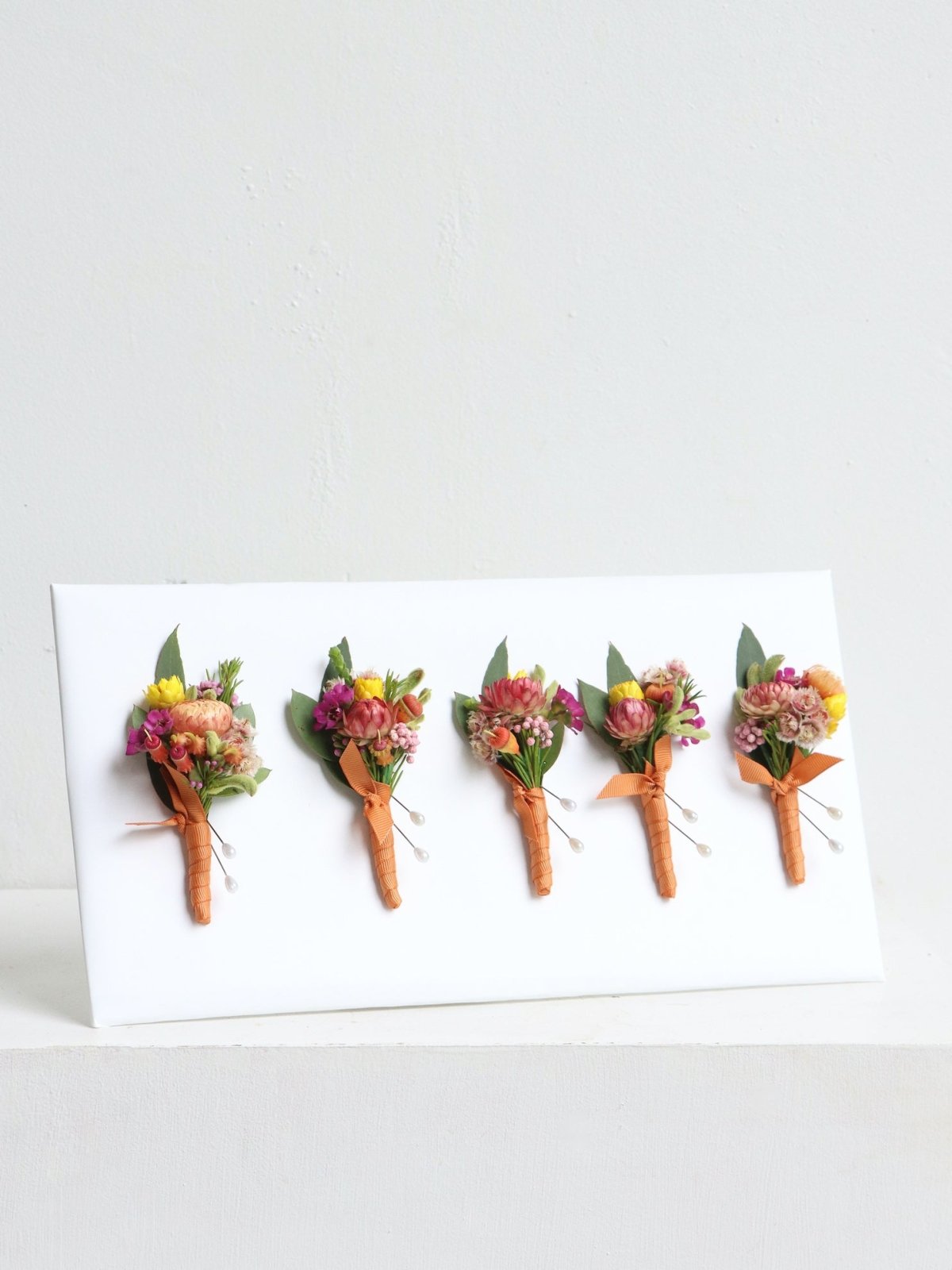 An example of native buttonholes. The buttonholes feature australian native banksia, orange flowering gum, yellow daisies, isopogon, purple waxflower, pink rice flower and melaleuca.