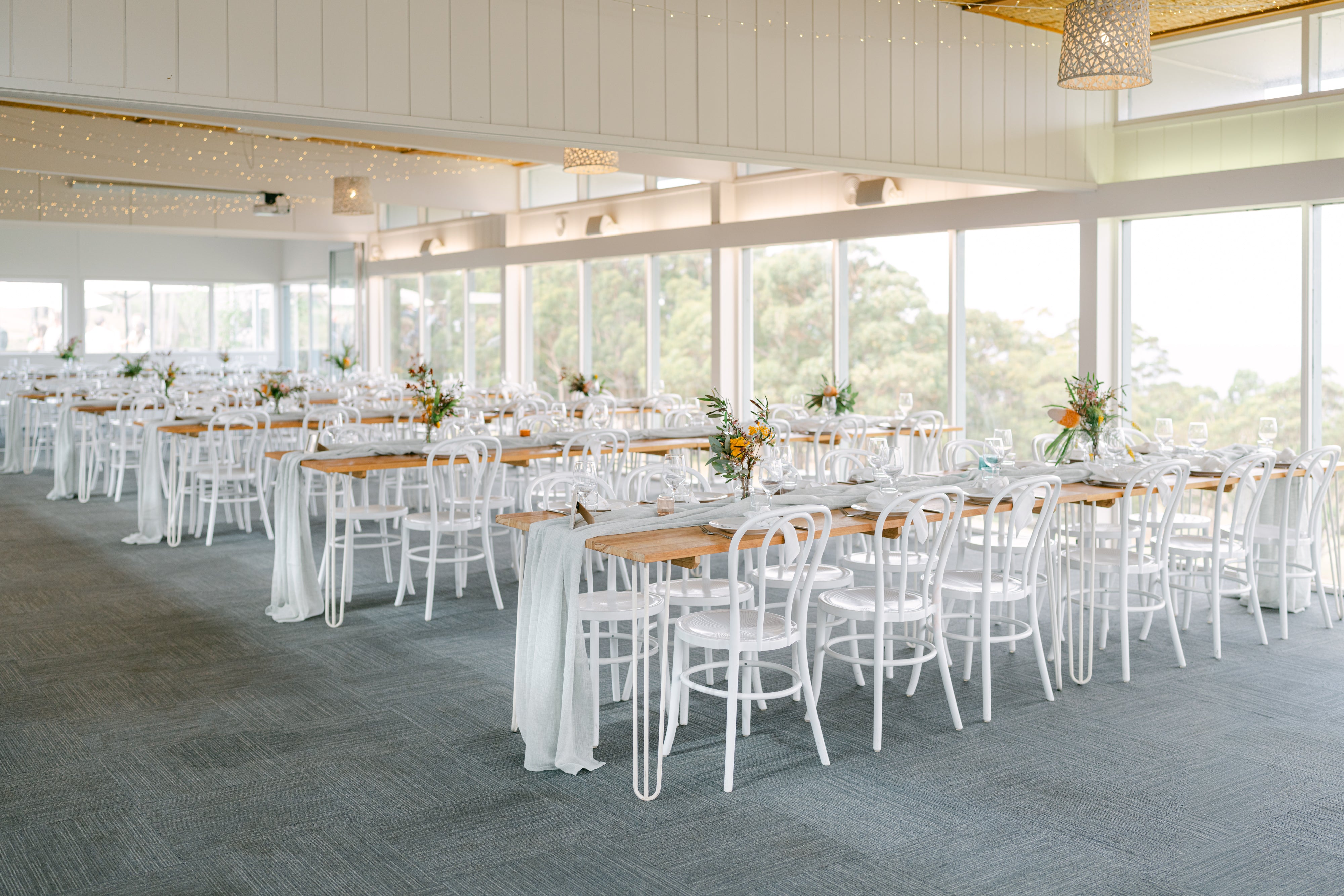 Large room with tables and chairs set up for an event, large windows allowing natural light.