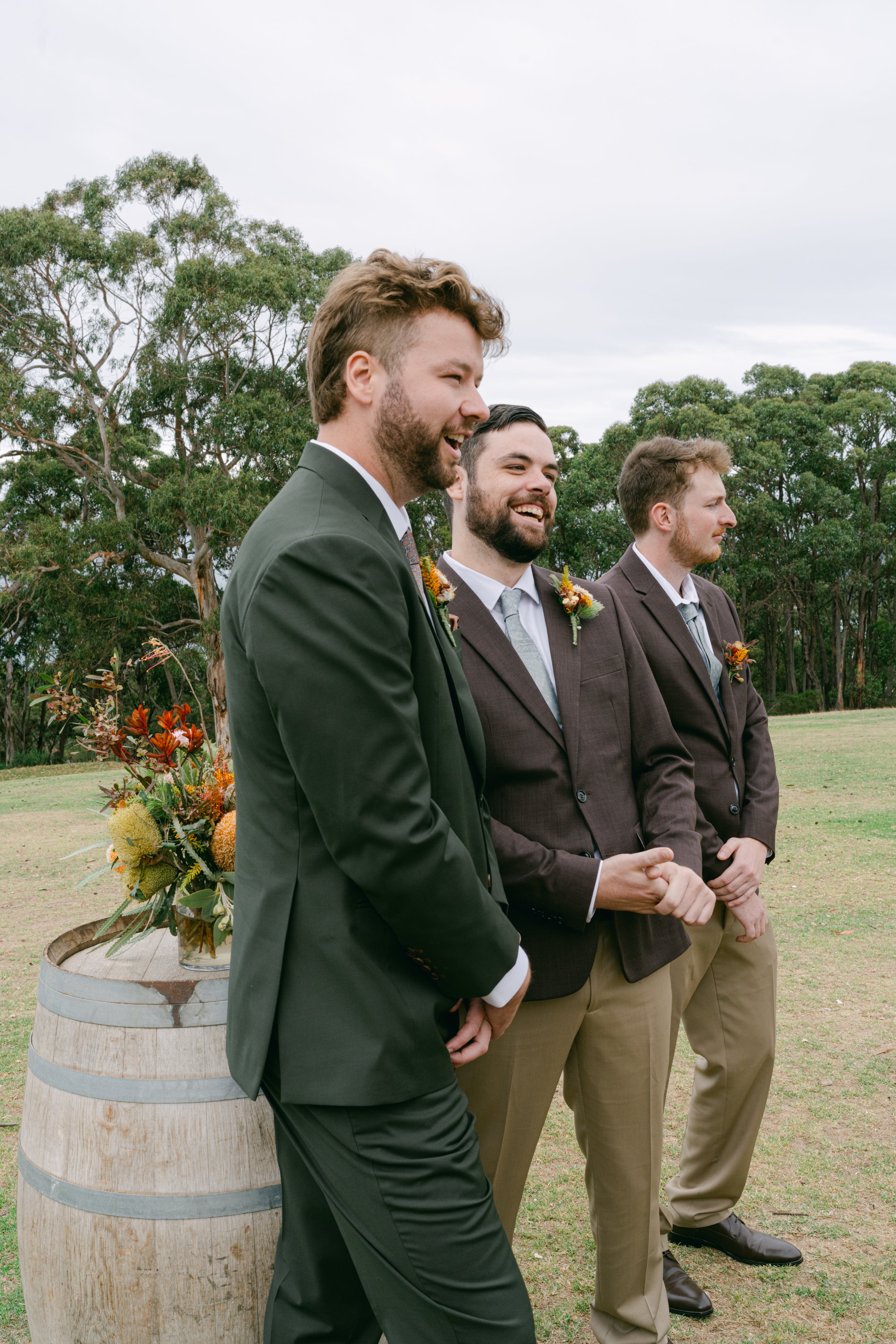 groom and groomsmen in suits standing outdoors with trees in the background