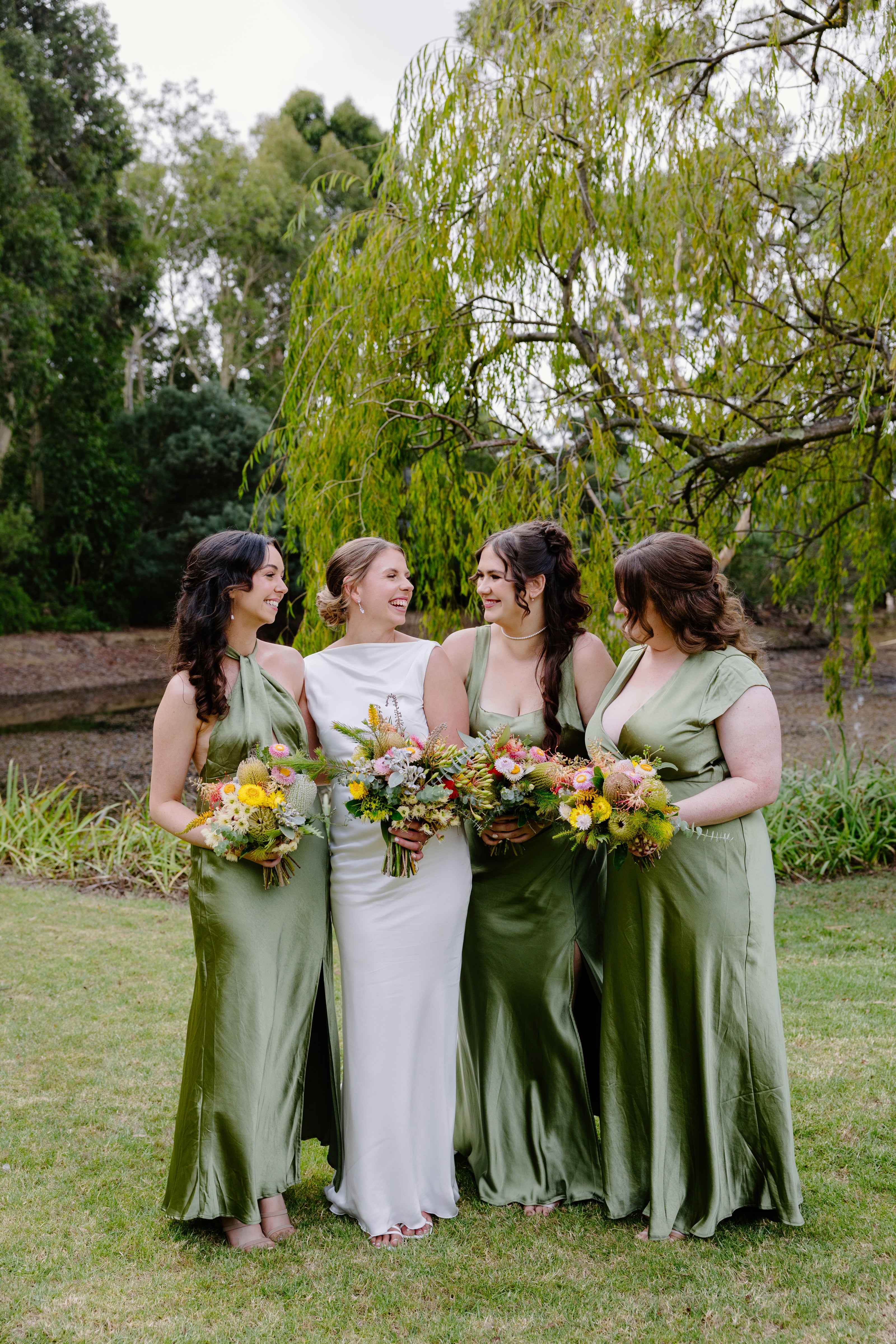 Bride and bridesmaids in green dresses standing outdoors with trees in the background