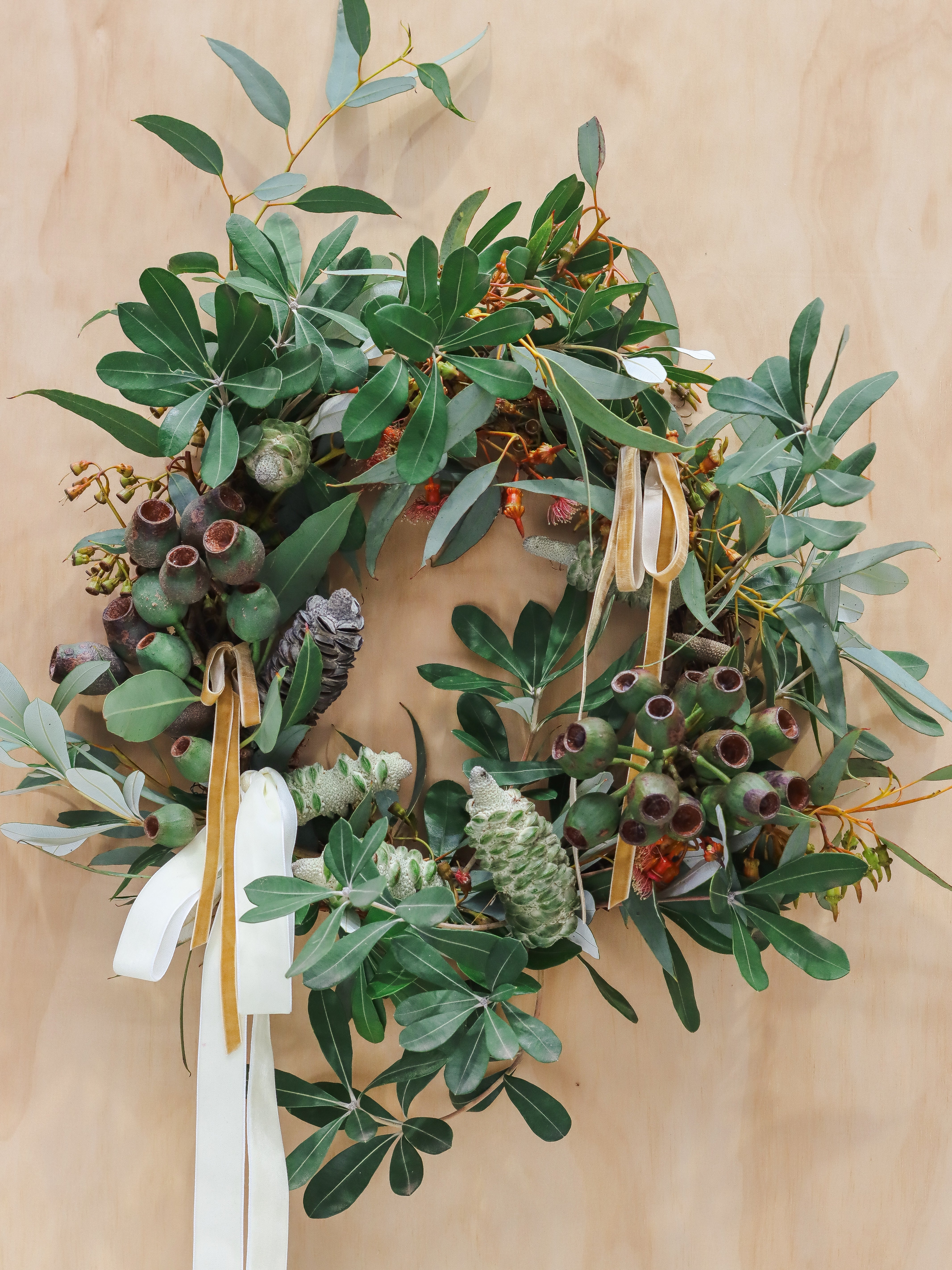Green leafy wreath with berries and ribbons on a beige background