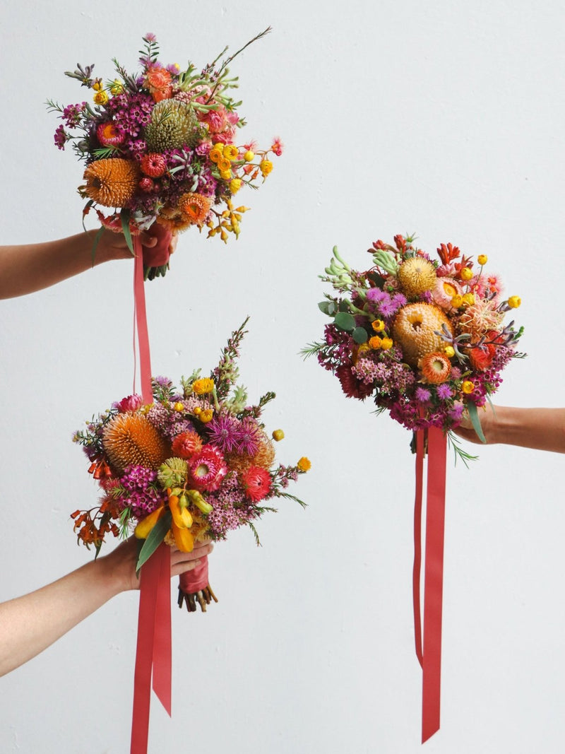 An example of native bridesmaids bouquets.  The bouquets feature australian native banksia, orange flowering gum, yellow daisies, isopogon, purple waxflower, pink rice flower and melaleuca.